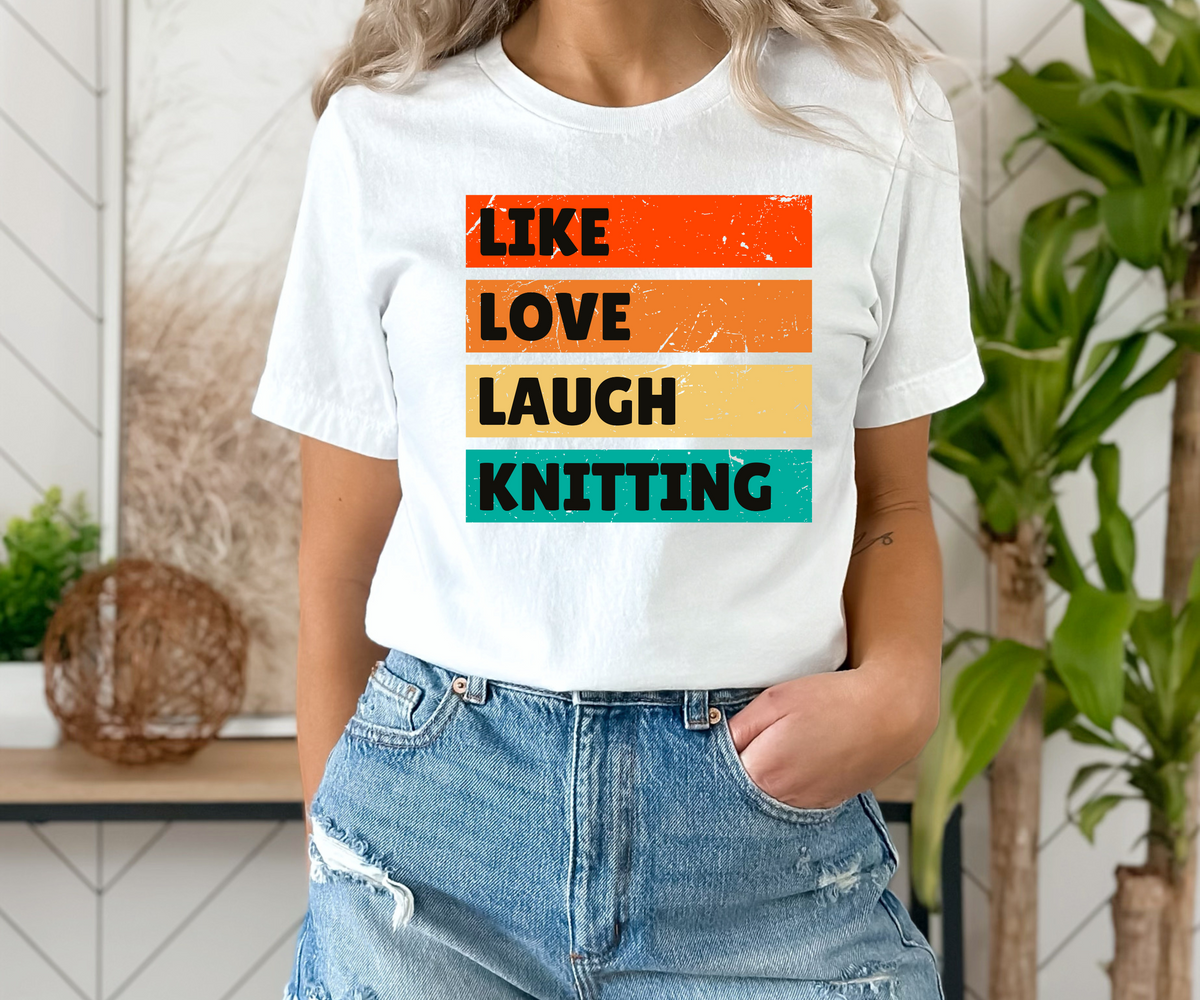 A woman wearing a white graphic t-shirt with the words 'LIKE LOVE LAUGH KNITTING' printed in black text over four horizontal color blocks (orange, light orange, yellow, teal), paired with distressed blue jeans.